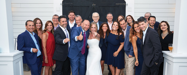Group of people pose around a groom giving a thumbs up and a bride pointing at the camera.